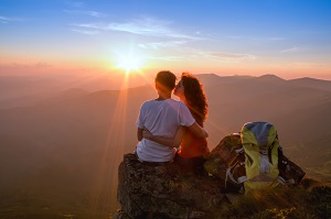 Happy couple hugging on a mountaintop at sunset